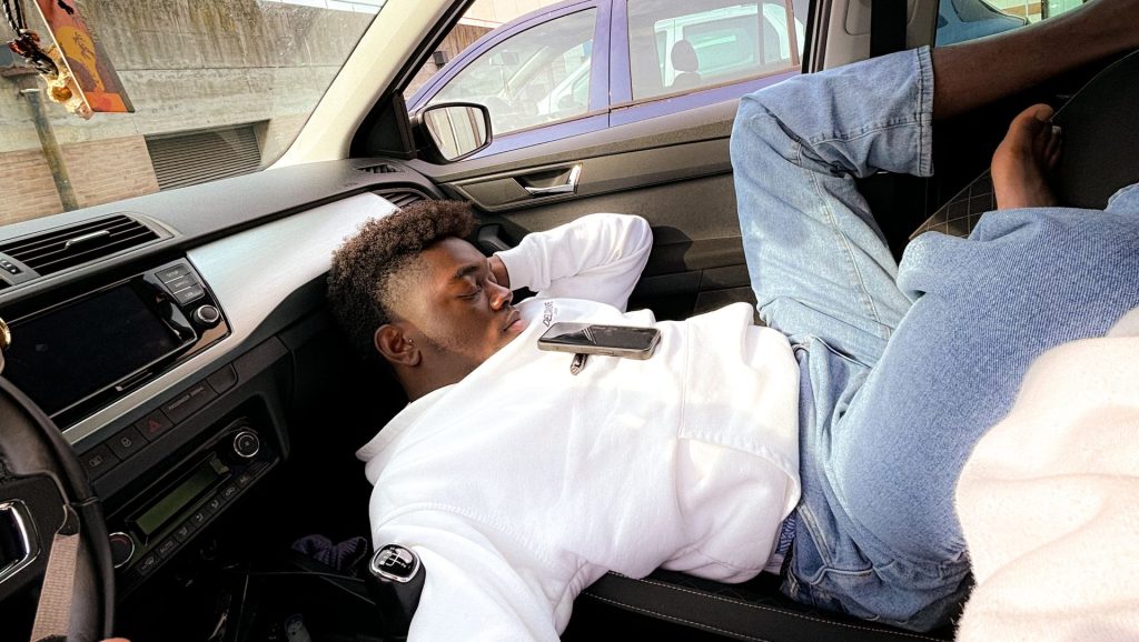 A man sleeping in a car interior, lying down with a smartphone on his chest