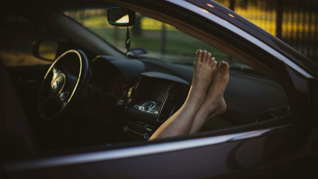 Bare feet propped up on a car dashboard looking out through the front windshield on a sunny day