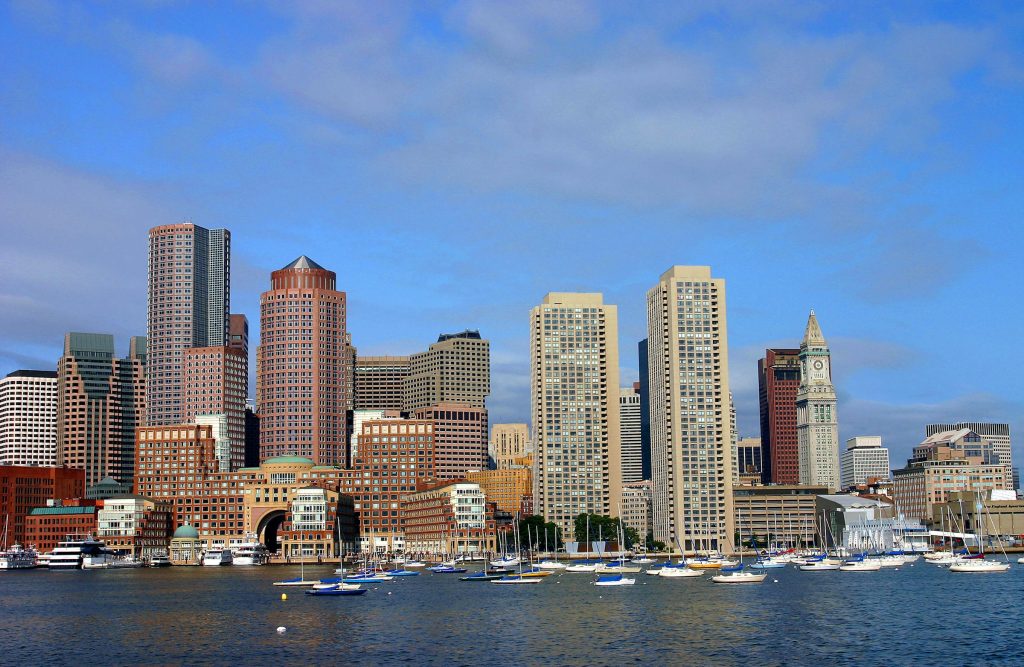 Boston Harbor skyline with boats docked in the foreground and the Custom House Tower under a clear blue sk
