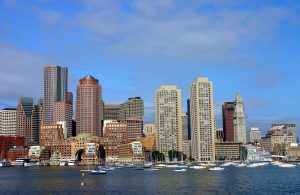 Boston Harbor skyline with boats docked in the foreground and the Custom House Tower under a clear blue sk