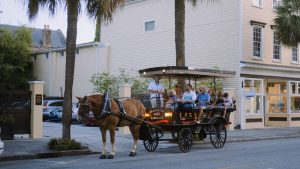 Horse-drawn carriage carrying tourists past historic pastel buildings and palm trees in Charleston, South Carolina