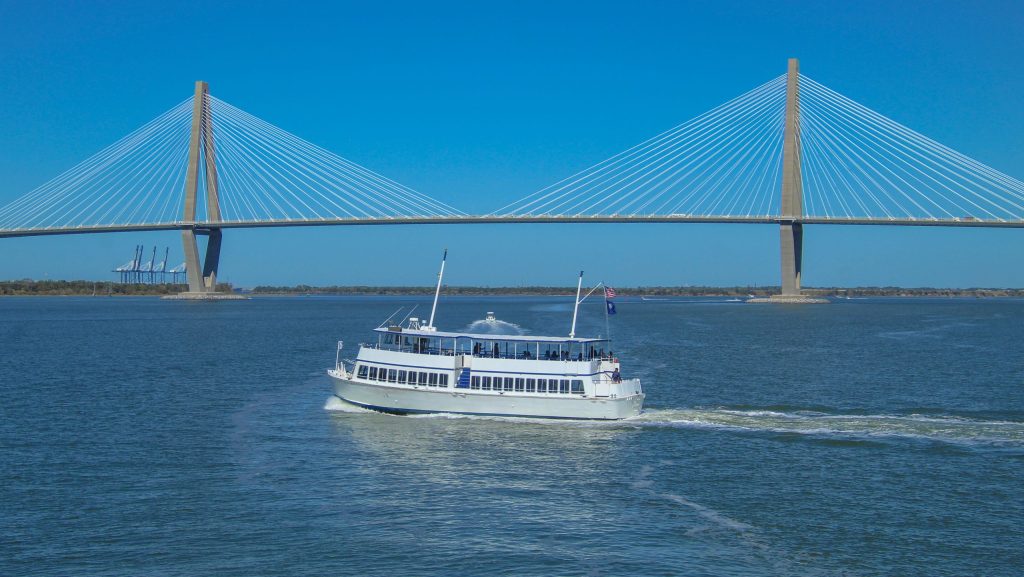 A white passenger ferry boat sailing on the water near the modern Arthur Ravenel Jr. Bridge in Charleston, South Carolina