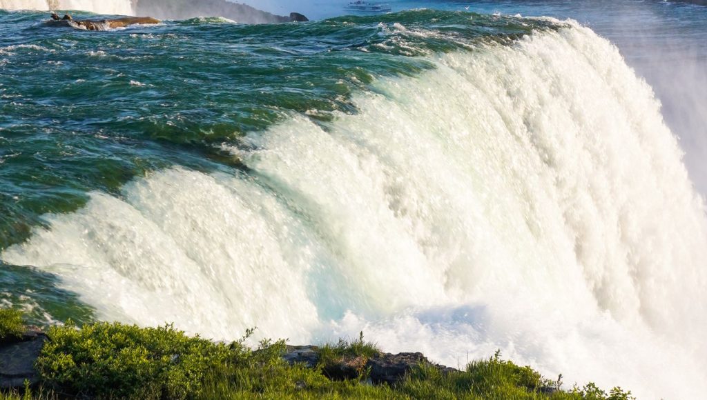 Cascading waters of Niagara Falls at Goat Island with mist rising and Canadian hotel skyline in the background